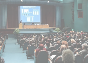 Множество людей сидят в аудитории и смотрят презентацию на проекторе